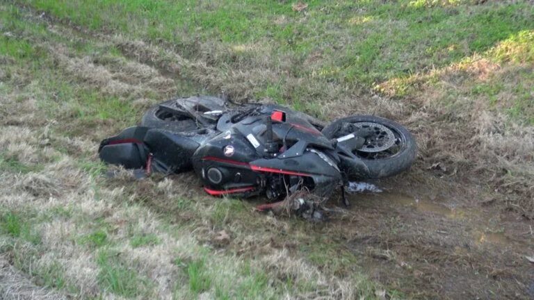 Crashed black motorcycle lying on muddy grass.