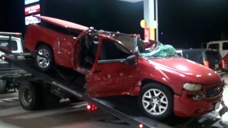 Wrecked red pickup truck being loaded onto a tow truck at night.