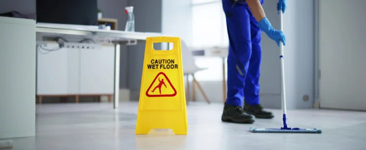 Janitor mopping a floor in the office with a caution sign, trying to prevent a slip and fall accident